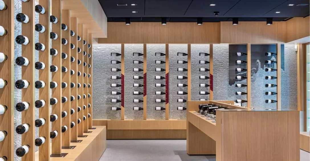 Modern interieur van de wijnwinkel/proeverijruimte van Valle Isarco in Zuid-Tirol. Lichte houten wanden en balies met honderden flessen wijn netjes uitgestald in houten rekken en op verlichte planken. Hedendaagse, warme inrichting met sfeerverlichting en een proeverijbalie op de voorgrond.