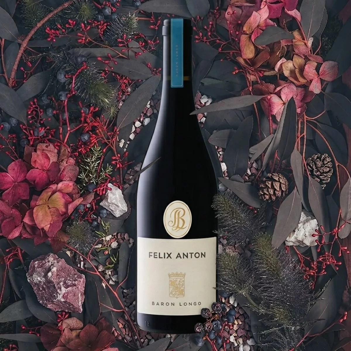 Fles Baron Longo Felix Anton Rosso liggend tussen gedroogde bloemen, bosbessen en dennenappels